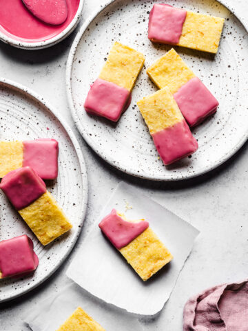 Cornmeal bars dipped in pink glaze on white plates and white parchment squares