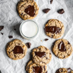 Top view of freshly baked coconut chocolate chip cookies with melted pools of chocolate with a glass of milk, resting on parchment paper