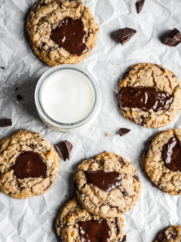 Top view of freshly baked coconut chocolate chip cookies with melted pools of chocolate with a glass of milk, resting on parchment paper