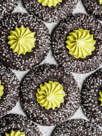 Chocolate thumbprint cookies rolled in sparkling sanding sugar, filled with a bright green piped mint matcha buttercream center.