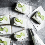 Squares of white cheesecake bars on parchment paper on a grey stone surface