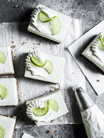 Squares of white cheesecake bars on parchment paper on a grey stone surface