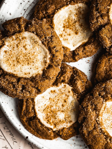 Pumpkin cookies with cream cheese centers on a white speckled ceramic platter. The cookies are dusted with cinnamon and coarse golden Turbinado sugar.