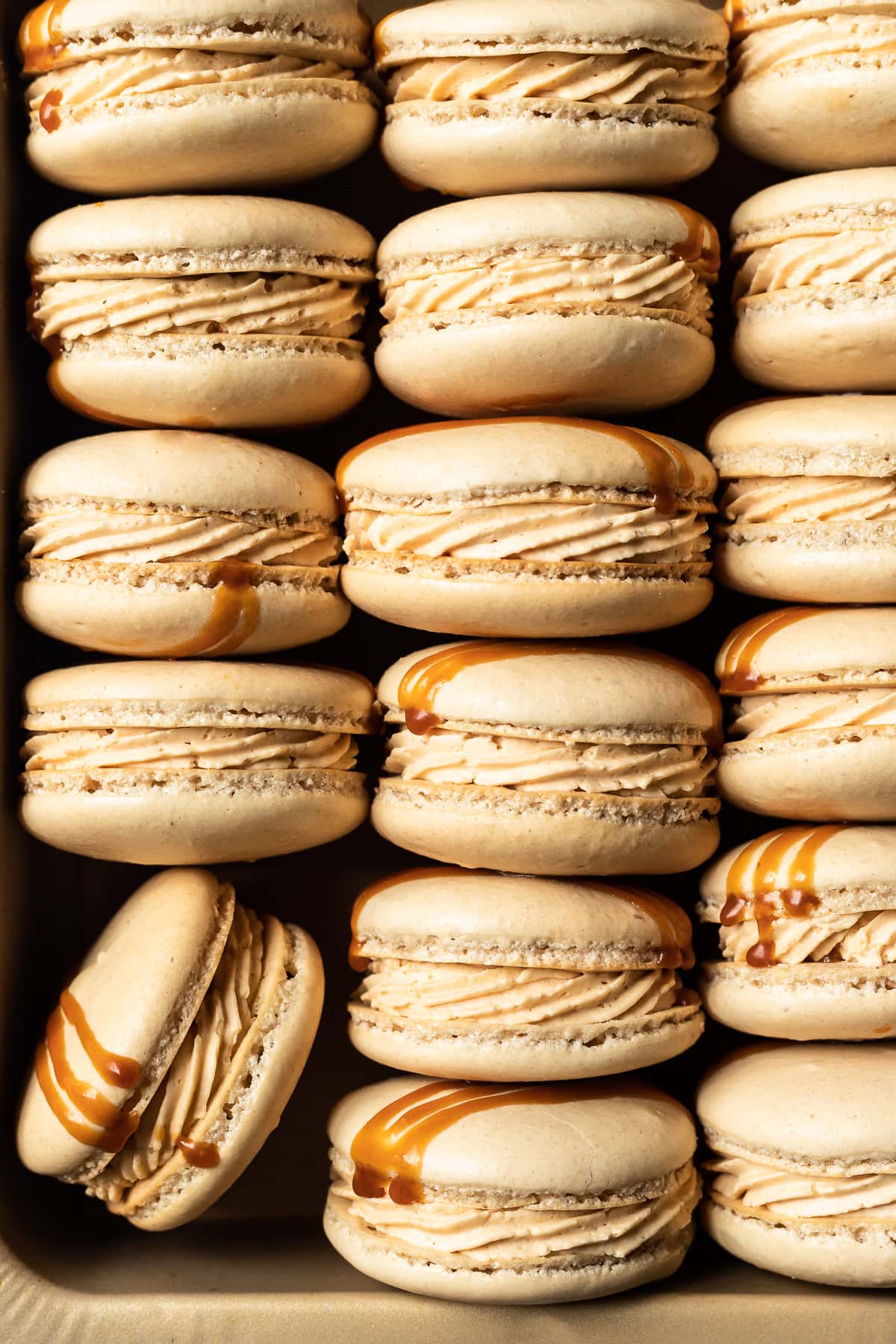 Close up view of salted caramel macarons tipped on their side and nestled into a gold metal pan.