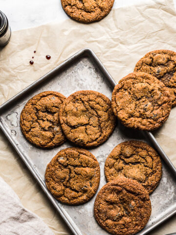 Ginger cookies on a baking sheet resting on a brown parchment paper rectangle. A jar of molasses is nearby.