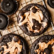 Three chocolate peanut butter cup cookies on a vintage metal cooling rack surrounded by wrapped and unwrapped chocolate peanut butter cups.