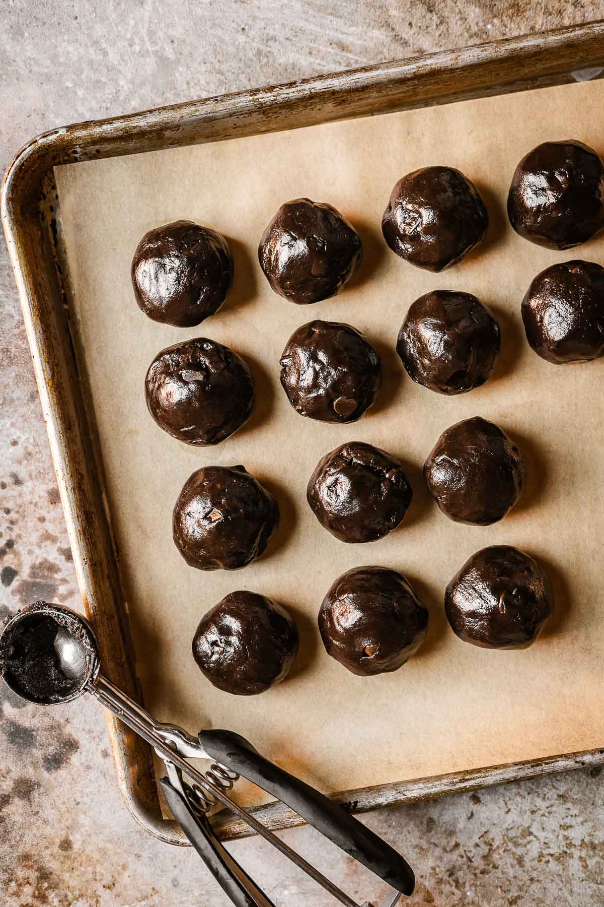 Balls of cookie dough on a parchment paper lined baking sheet. 