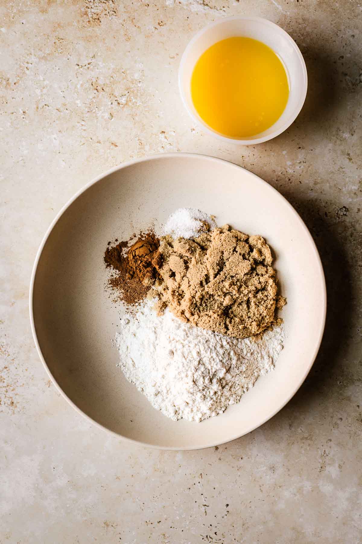 A low tan bowl filled with dry ingredients for streusel muffin topping, and a small white glass bowl with melted butter nearby.