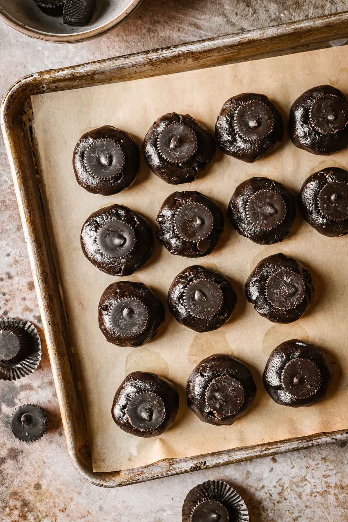 A baking sheet with cookie dough balls topped with peanut butter cups.