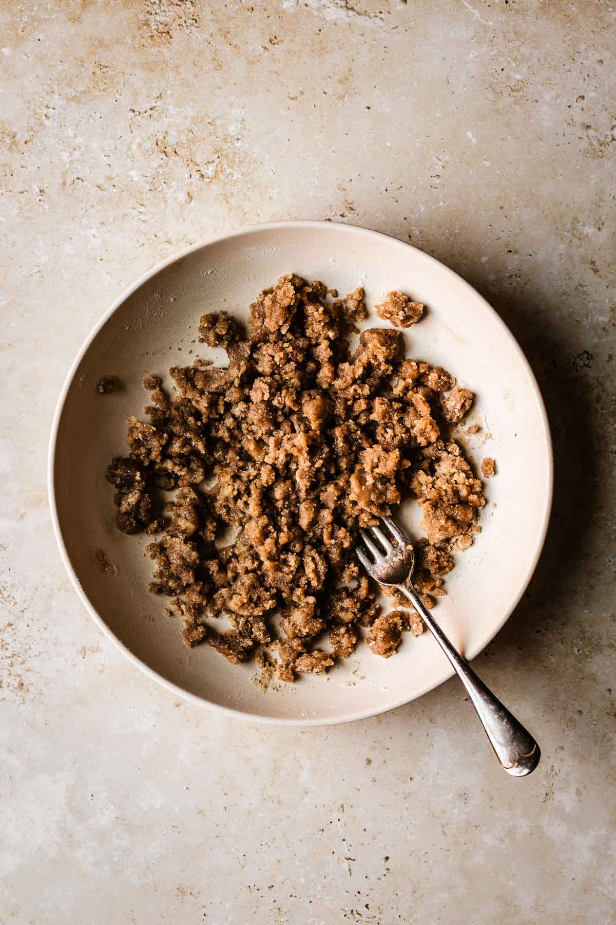 A shallow tan bowl with streusel topping for muffins. A fork rests in the bowl.