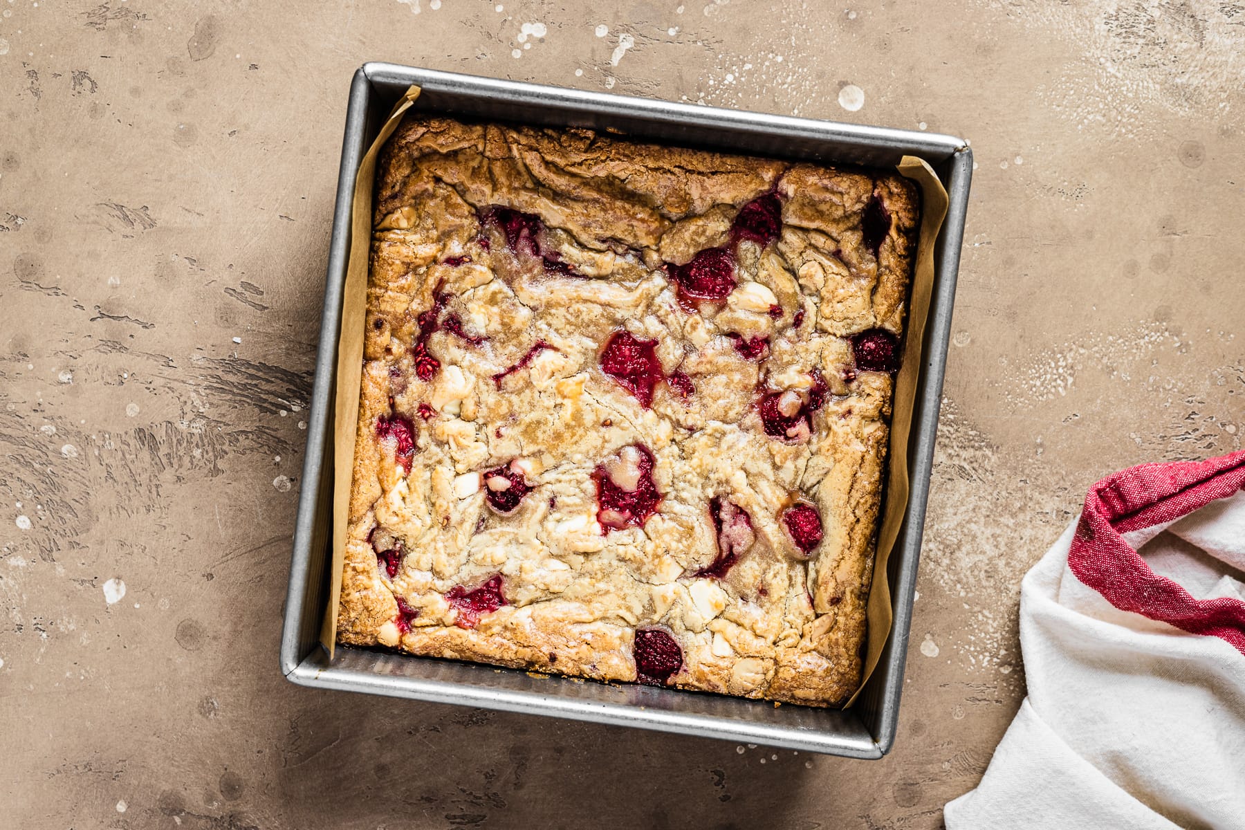 A square pan of baked blondies on a tan stone surface with a red and white napkin at bottom right.