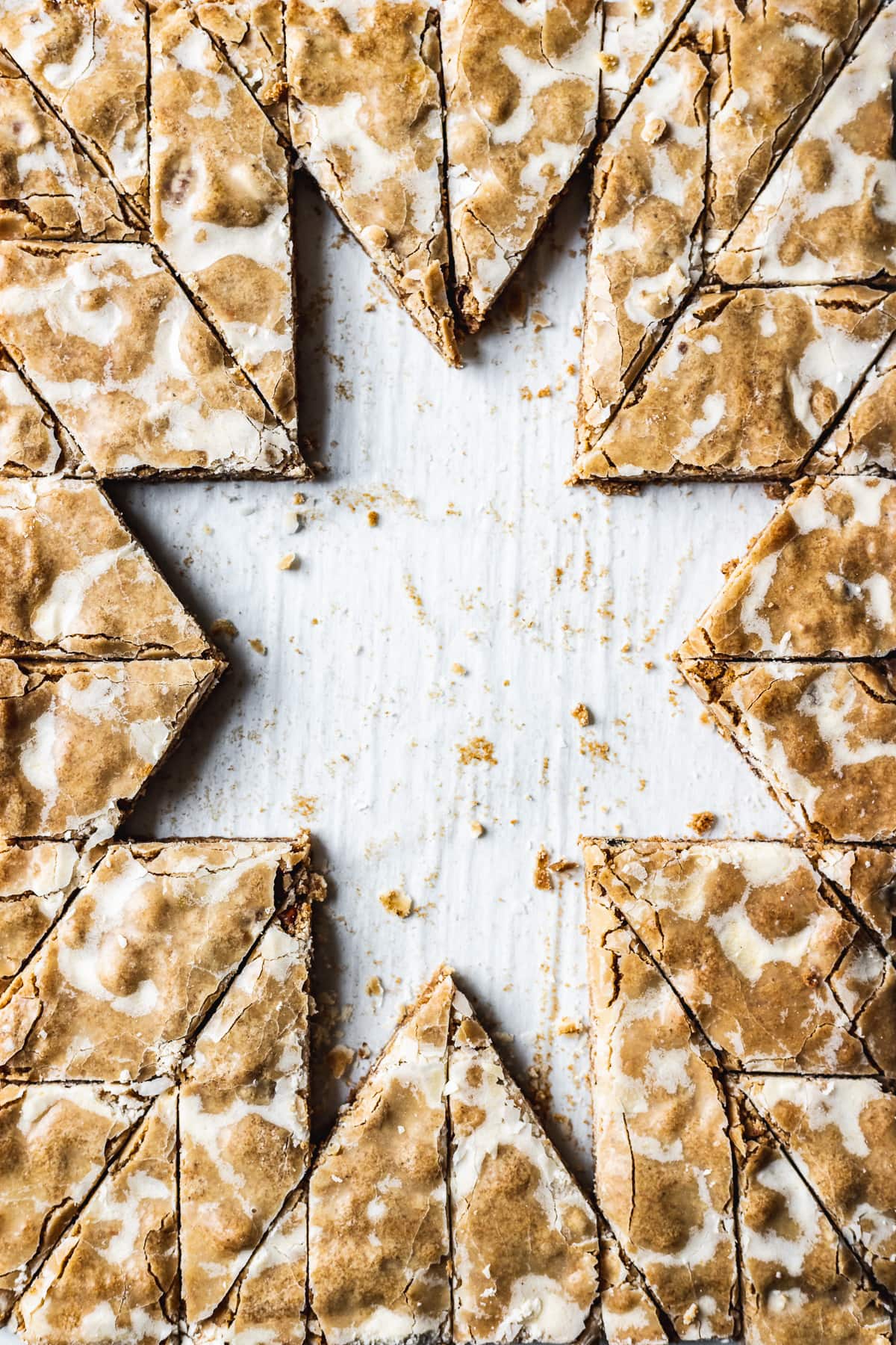 A closeup of bar cookies cut into a decorative holiday star pattern. The cookies in the middle have been removed, revealing the white parchment paper below in the shape of an eight pointed star.