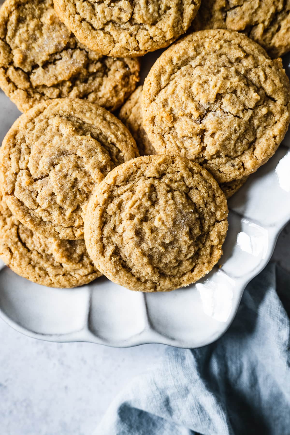 Peanut butter cookies on a fluted white ceramic serving plate. A light blue linen napkin peeks into the bottom right of the frame.