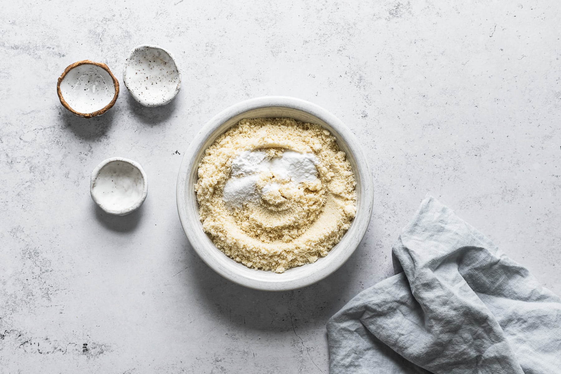 Process photo of cookie dough with dry ingredients mixed together in a white ceramic bowl on a white stone surface.