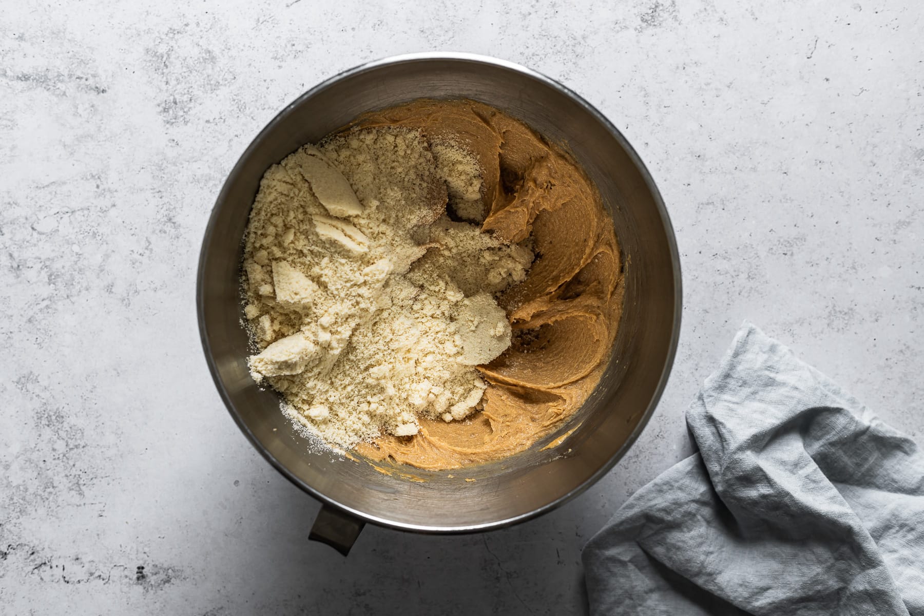 A process photo showing dry ingredients added to a mixing bowl of cookie batter.