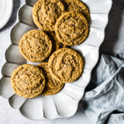 Peanut butter cookies on a fluted white ceramic serving plate. The plate rests on a white stone surface with a light blue linen napkin nearby.