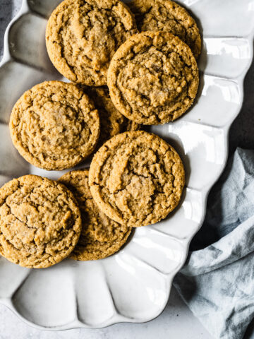 Peanut butter cookies on a fluted white ceramic serving plate. The plate rests on a white stone surface with a light blue linen napkin nearby.