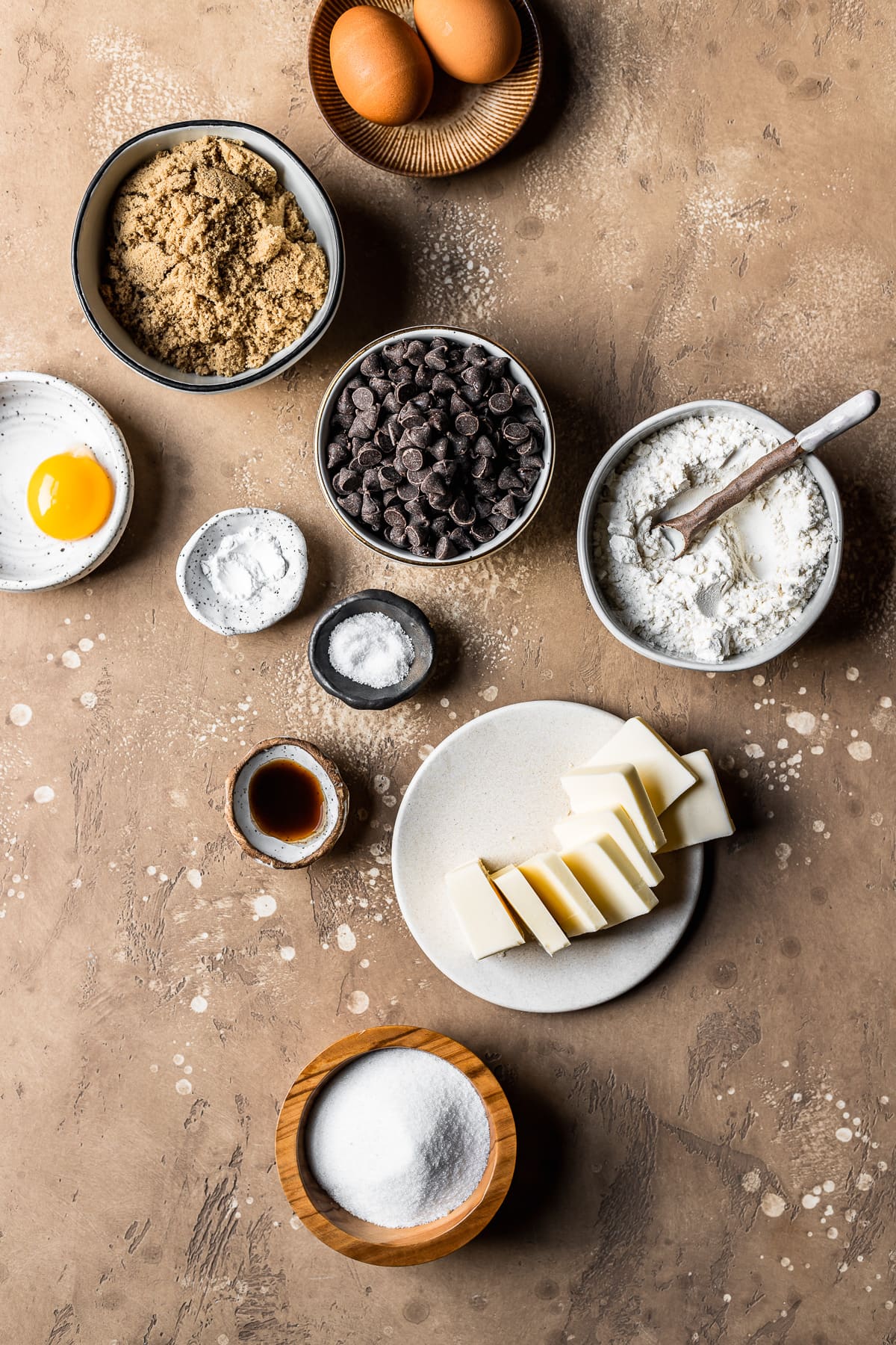 Various small ceramic bowls hold the ingredients for brownie blondie bars. The bowls rest on a warm speckled tan stone surface.