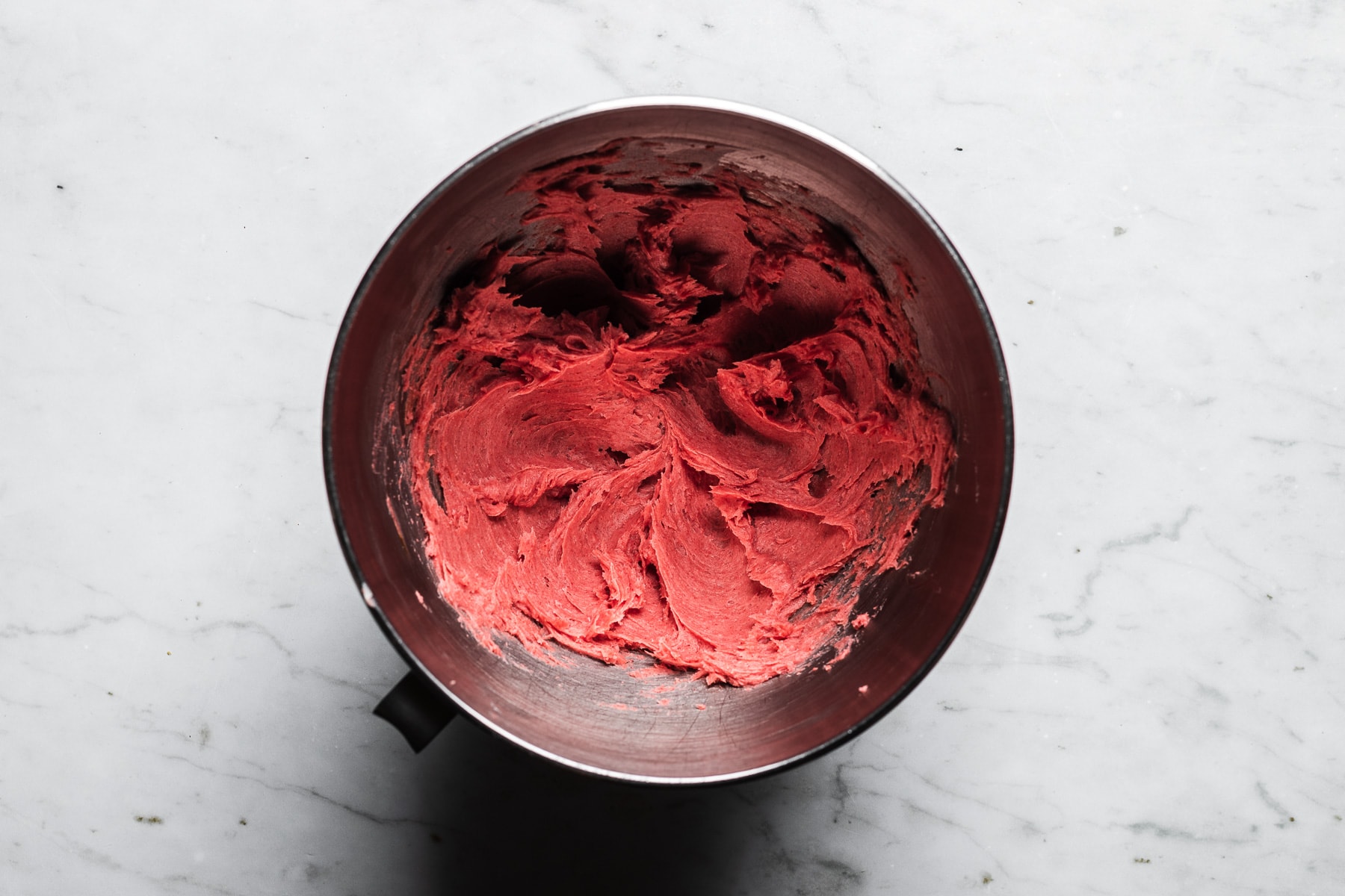 A process photo showing pink shortbread batter in a metal mixing bowl, resting on a light grey marble surface.