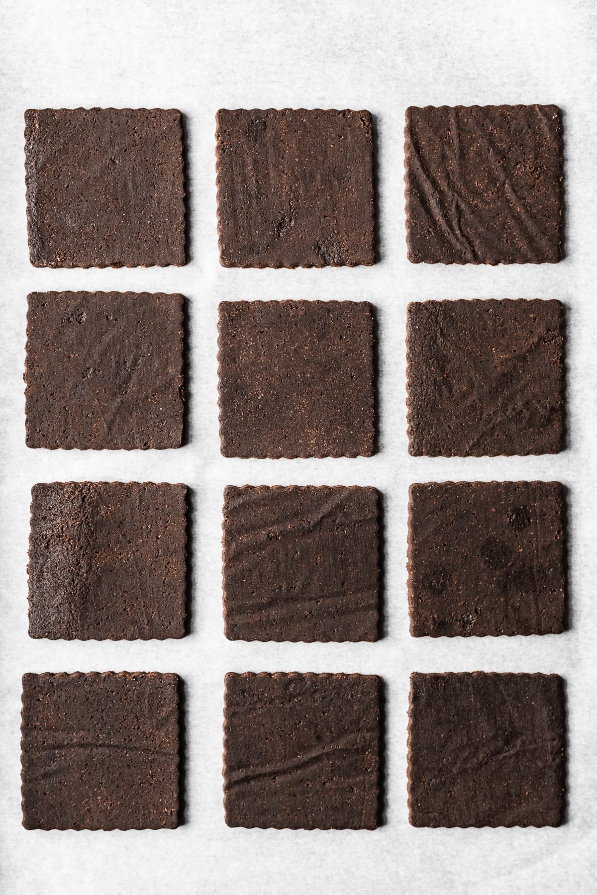 Three columns of unbaked cookie dough cutouts on white parchment paper.