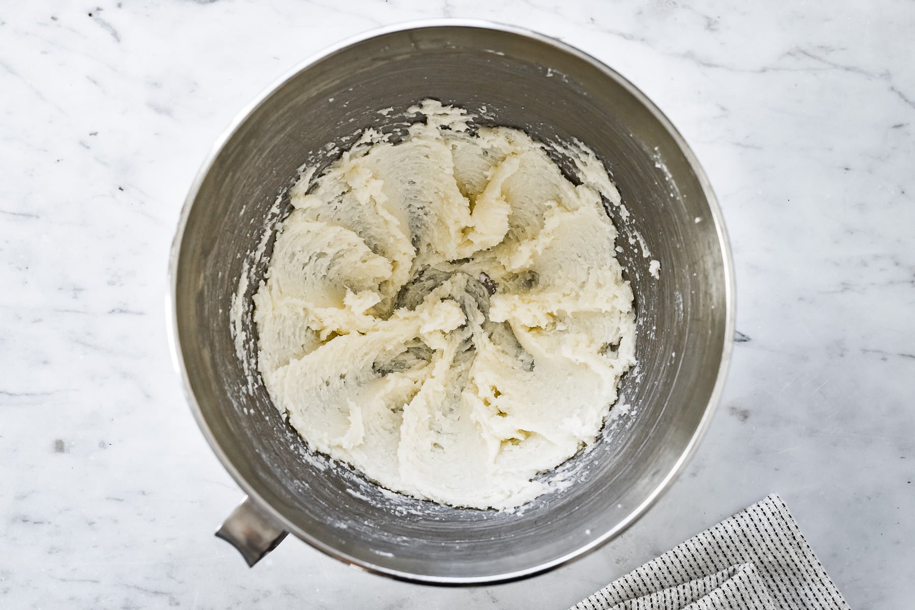 Process photo showing creamed butter and sugar for chocolate wafer dough in a mixing bowl on a marble surface.