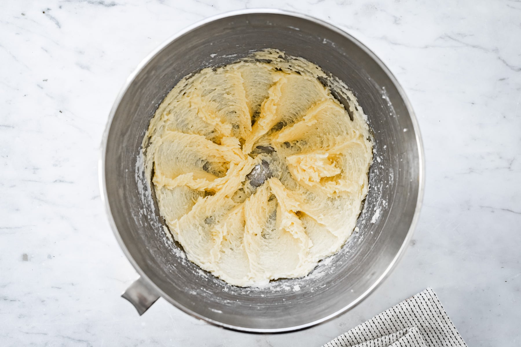 Process photo showing eggs and vanilla added to butter in a mixing bowl on a marble surface.