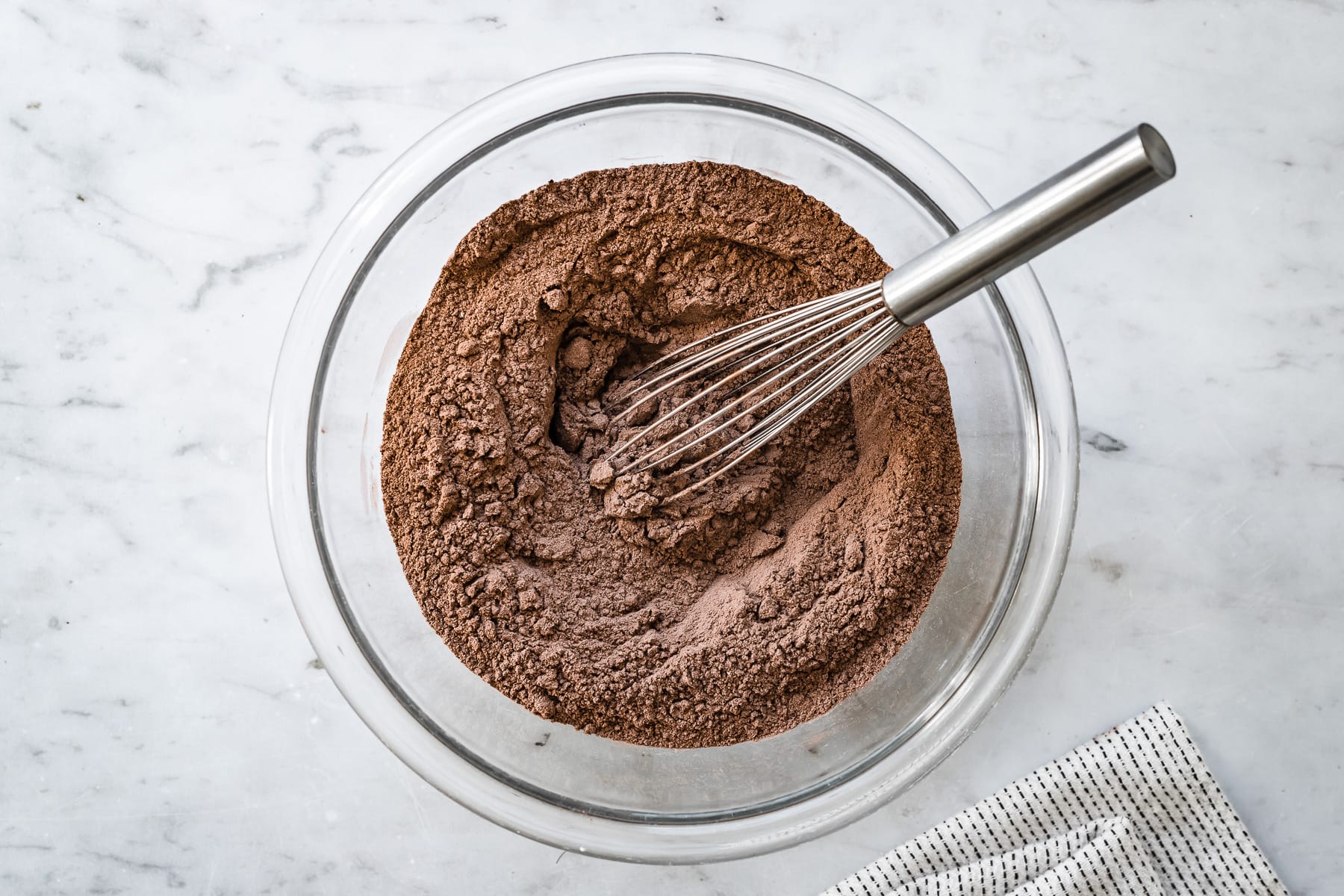 Process photo showing whisked dry ingedients for chocolate wafer cookies in a clear glass bowl on a marble surface.