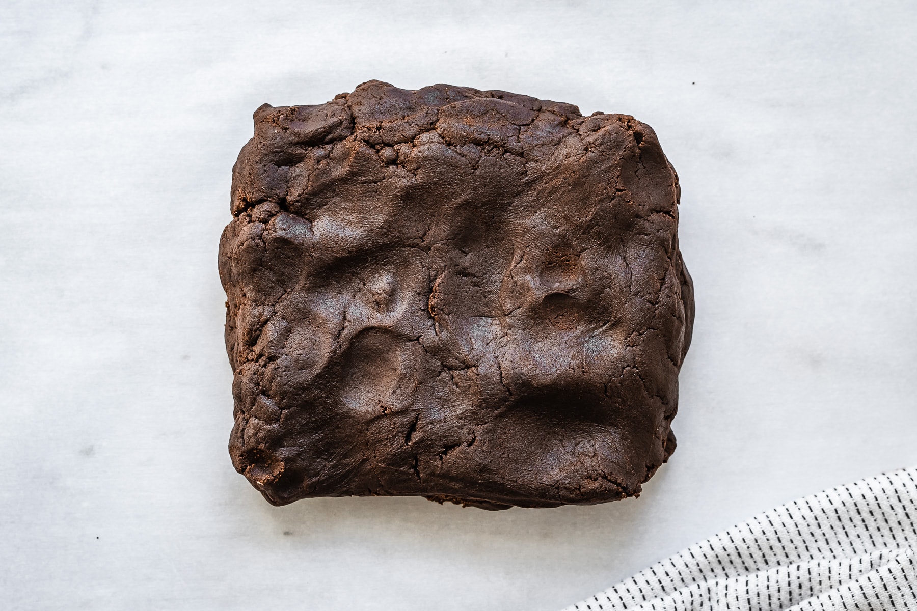 Process photo showing a rectangular slab of chocolate dough on a marble surface.