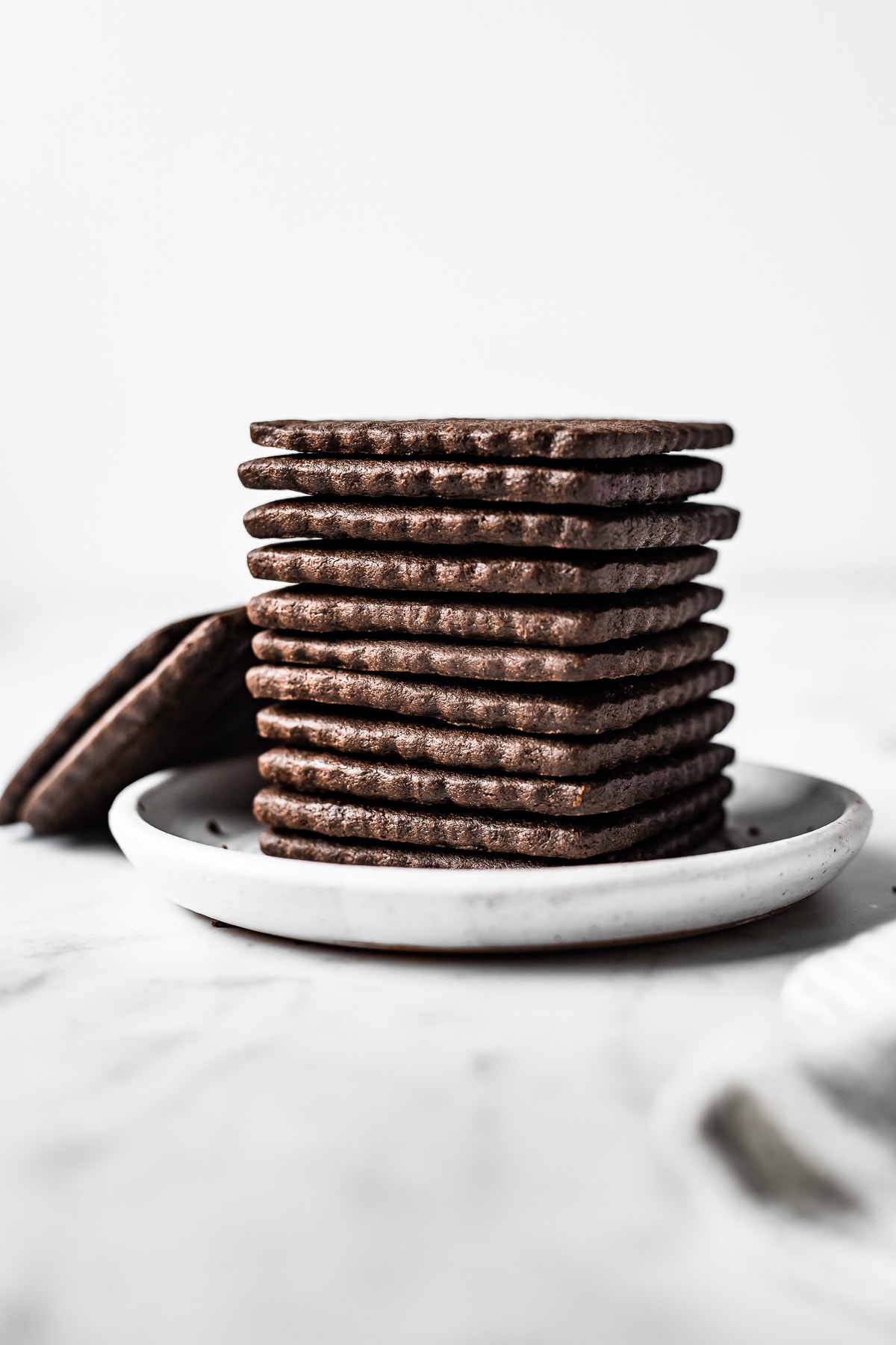 A stack of square chocolate cookies with scalloped edges on a small plate.