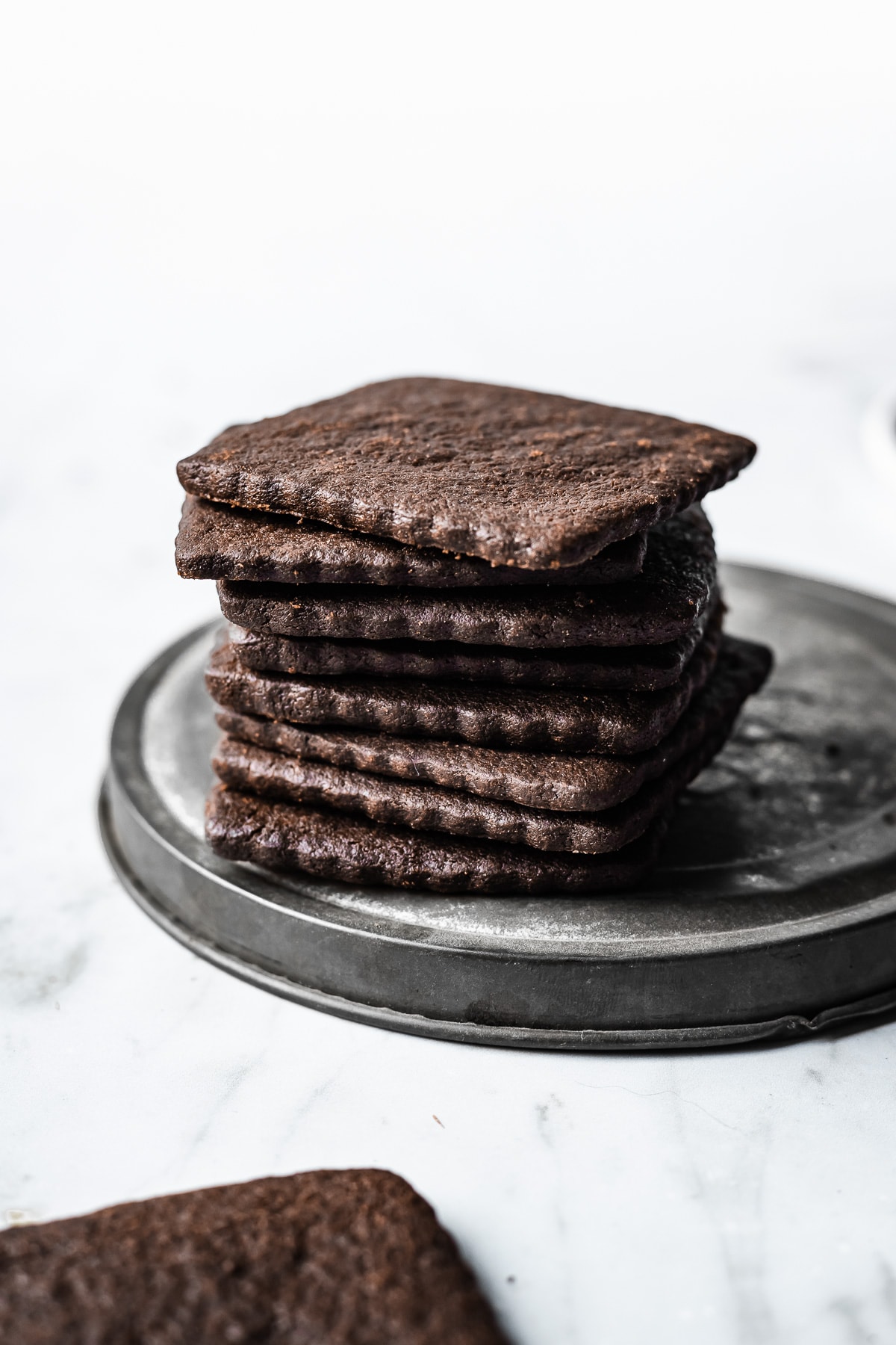 A stack of scalloped edged thin cookies on a vintage baking tin lid on a marble surface.