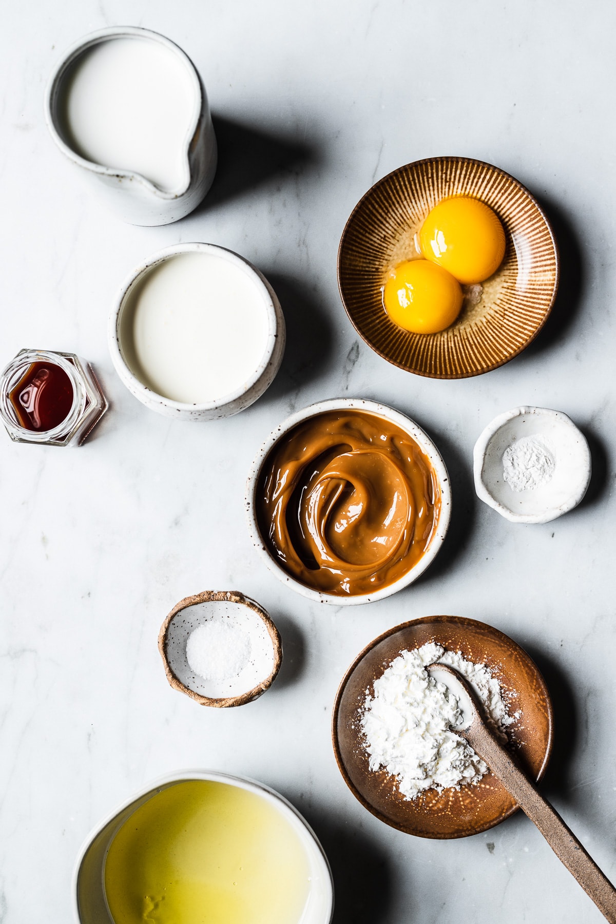 Process photo showing ingredients to make dulce de leche mousse organized in containers on a marble surface.