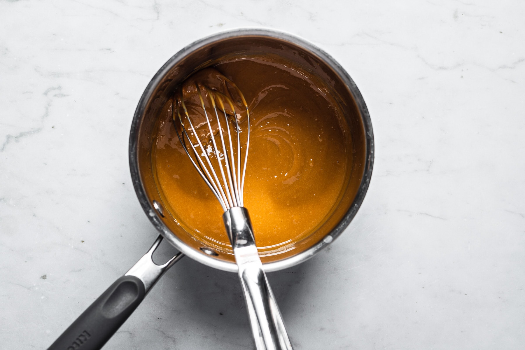 Process photo showing dulce de leche and eggs being mixed in a saucepot with a whisk.