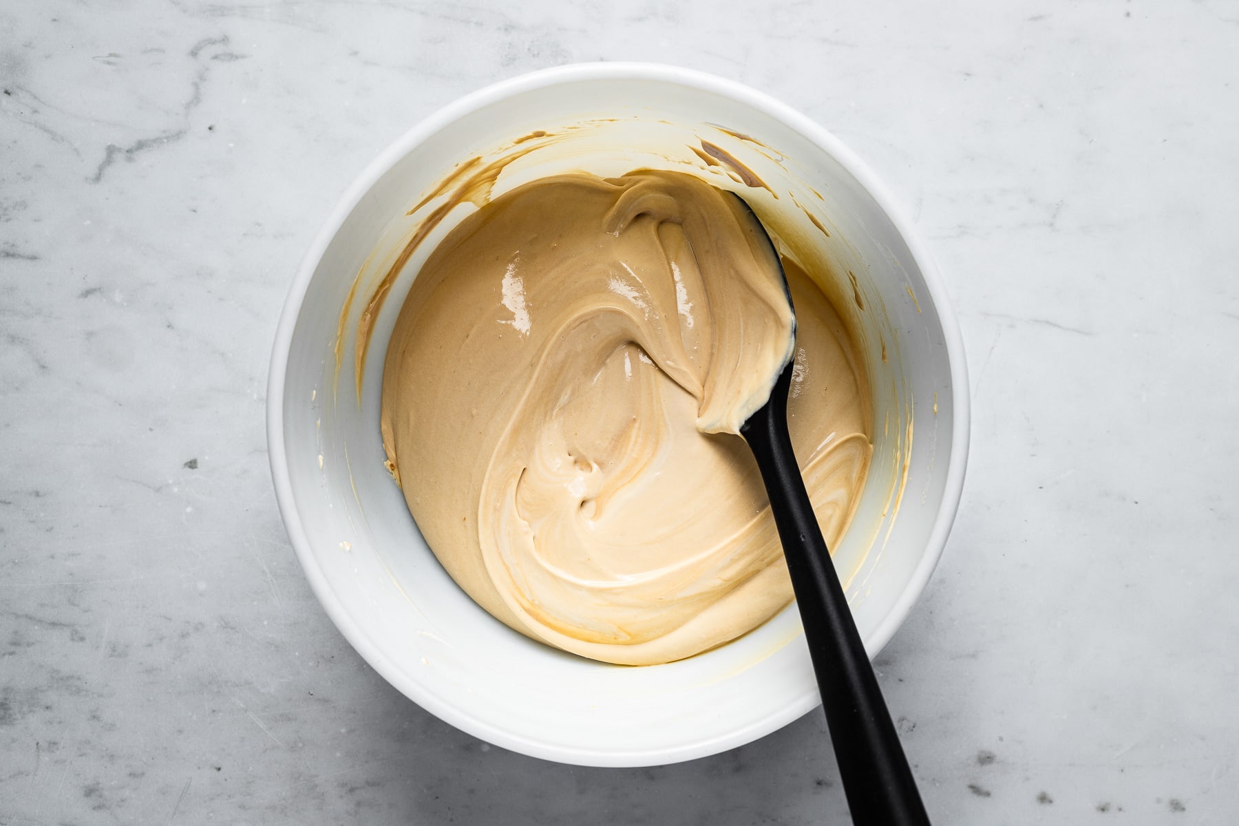 A process photo of a white bowl with softly whipped cream being folded into a bowl of pastry cream with a rubber spatula.