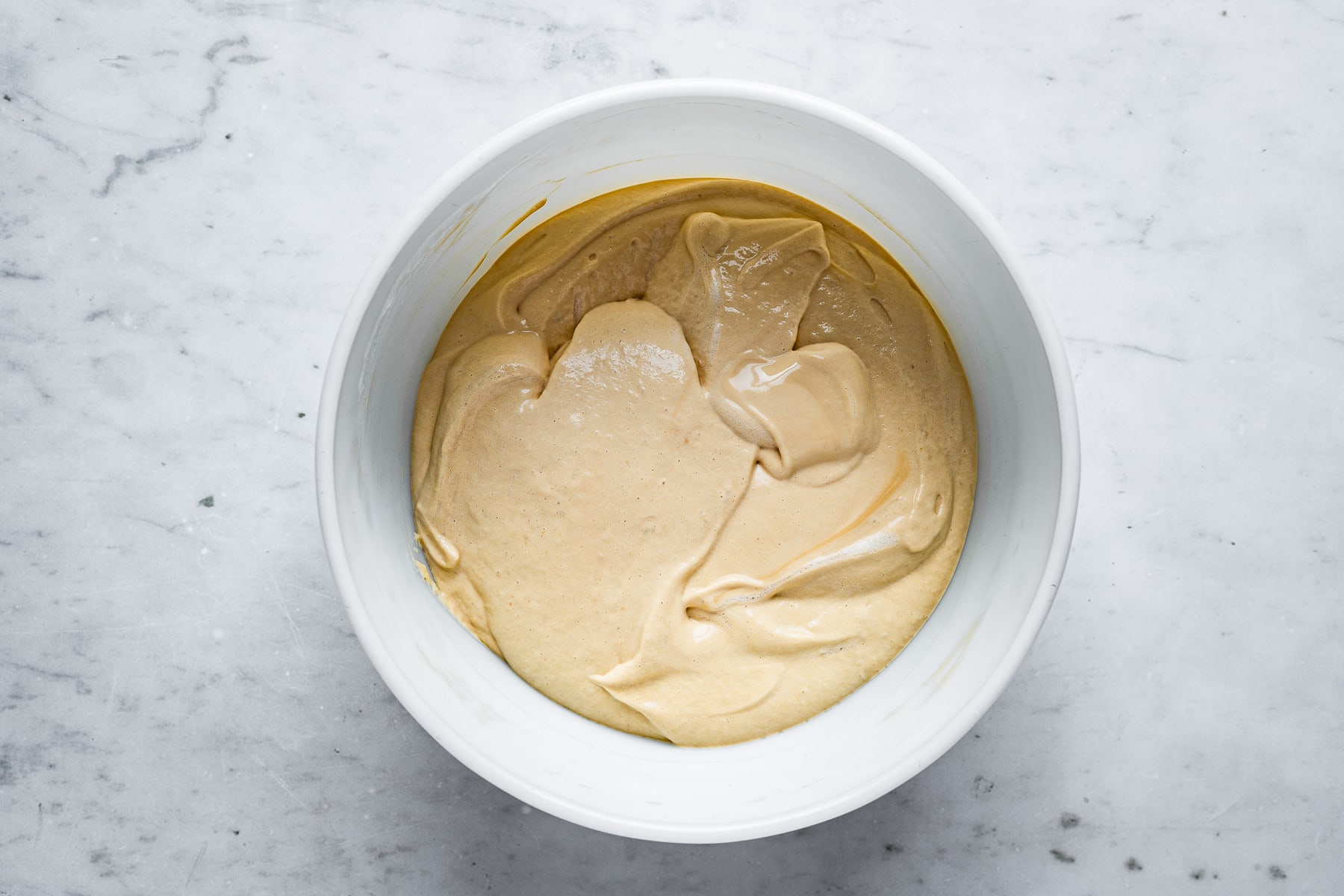 A process photo of a large white bowl of fully mixed dulce de leche mousse that has had the egg whites incorporated.