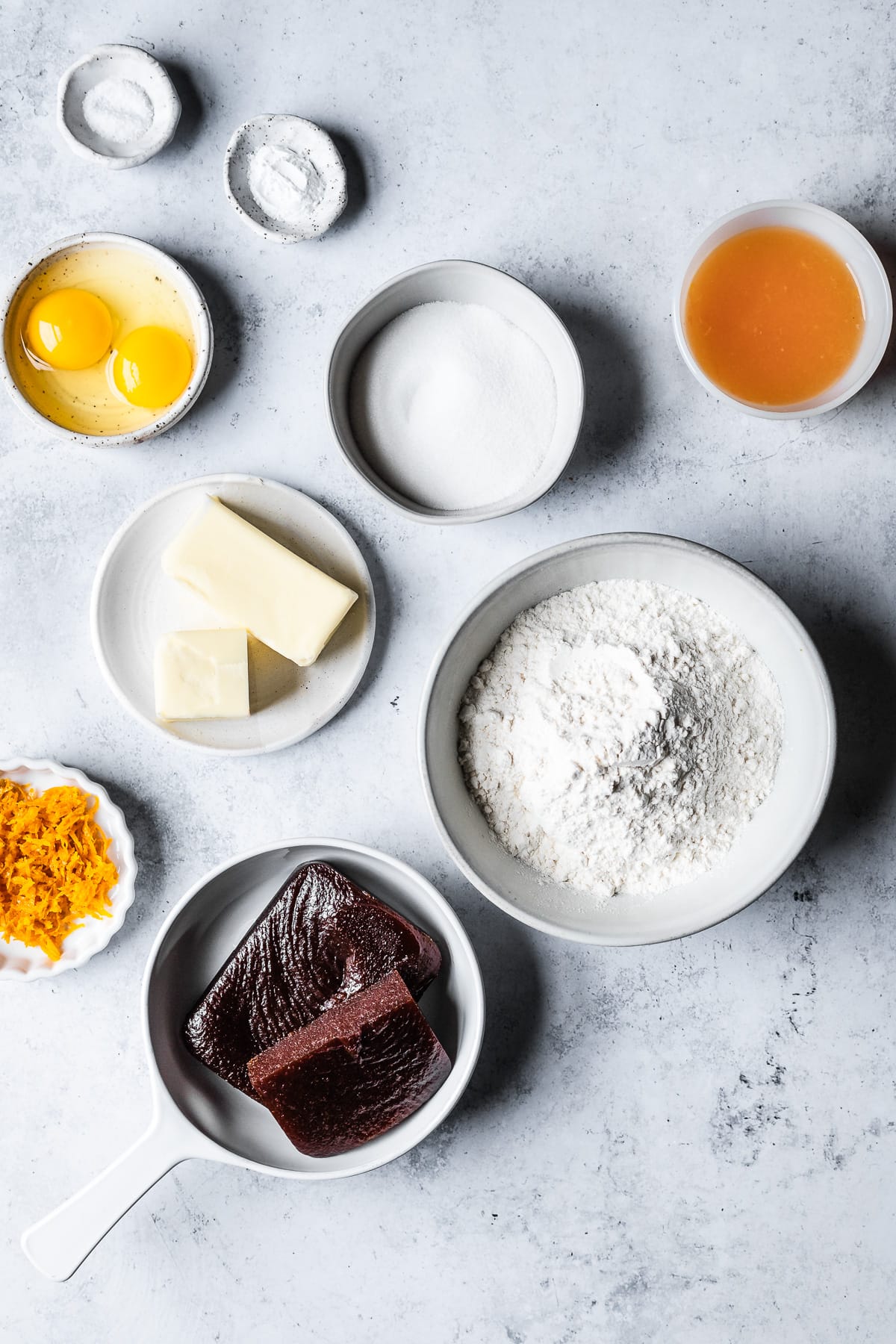 Ingredients for pasta frola in white ceramic bowls on a blue grey cement surface.