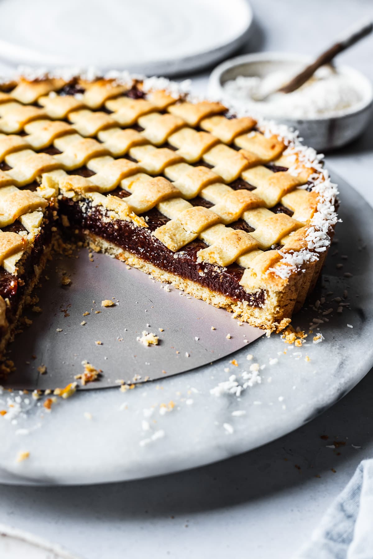 A quince tart with lattice top and border of dessicated coconut. There are a few slices missing, revealing the base crust and filling.