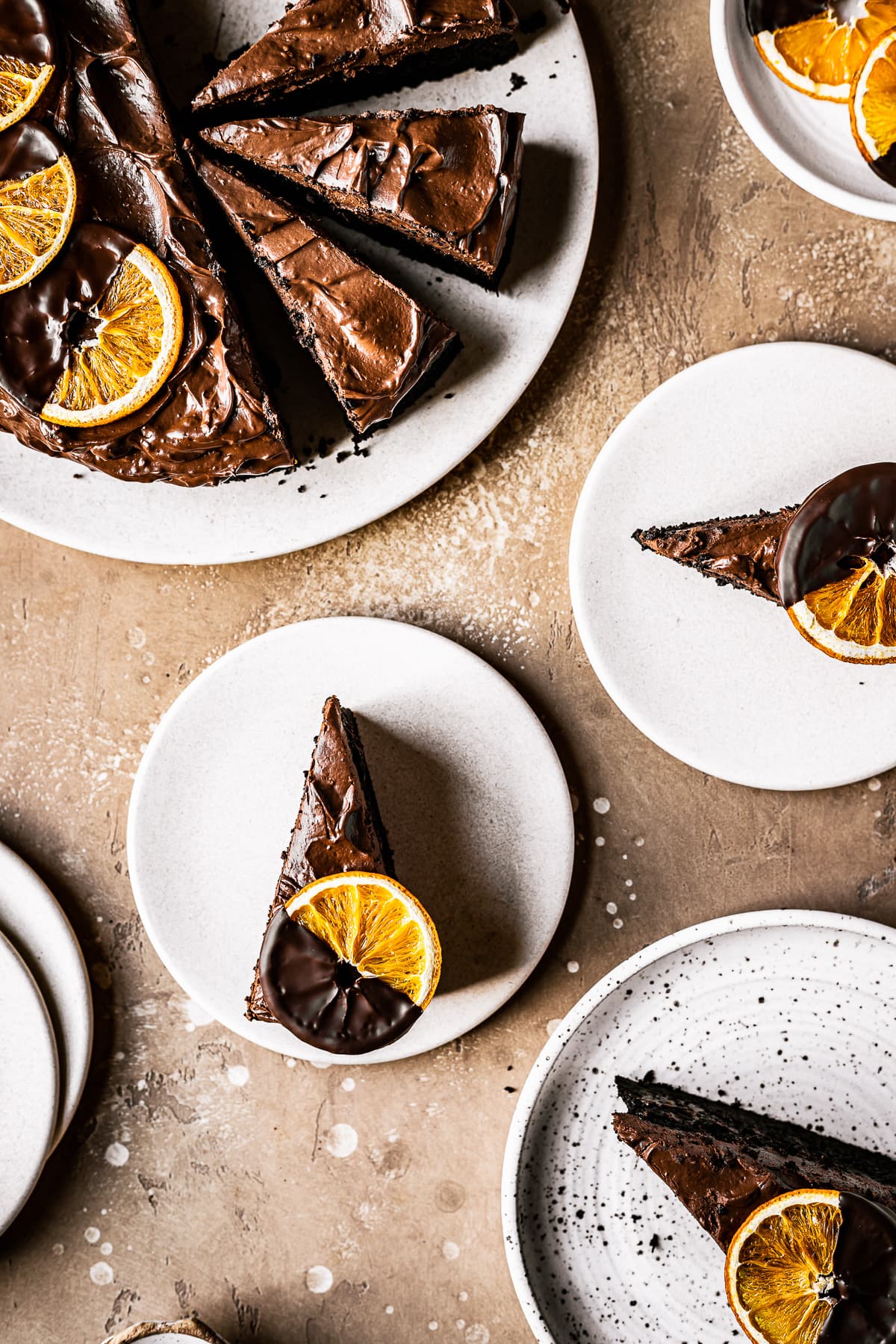 Slices of chocolate orange cake on plates with a large serving platter of additional cake nearby.