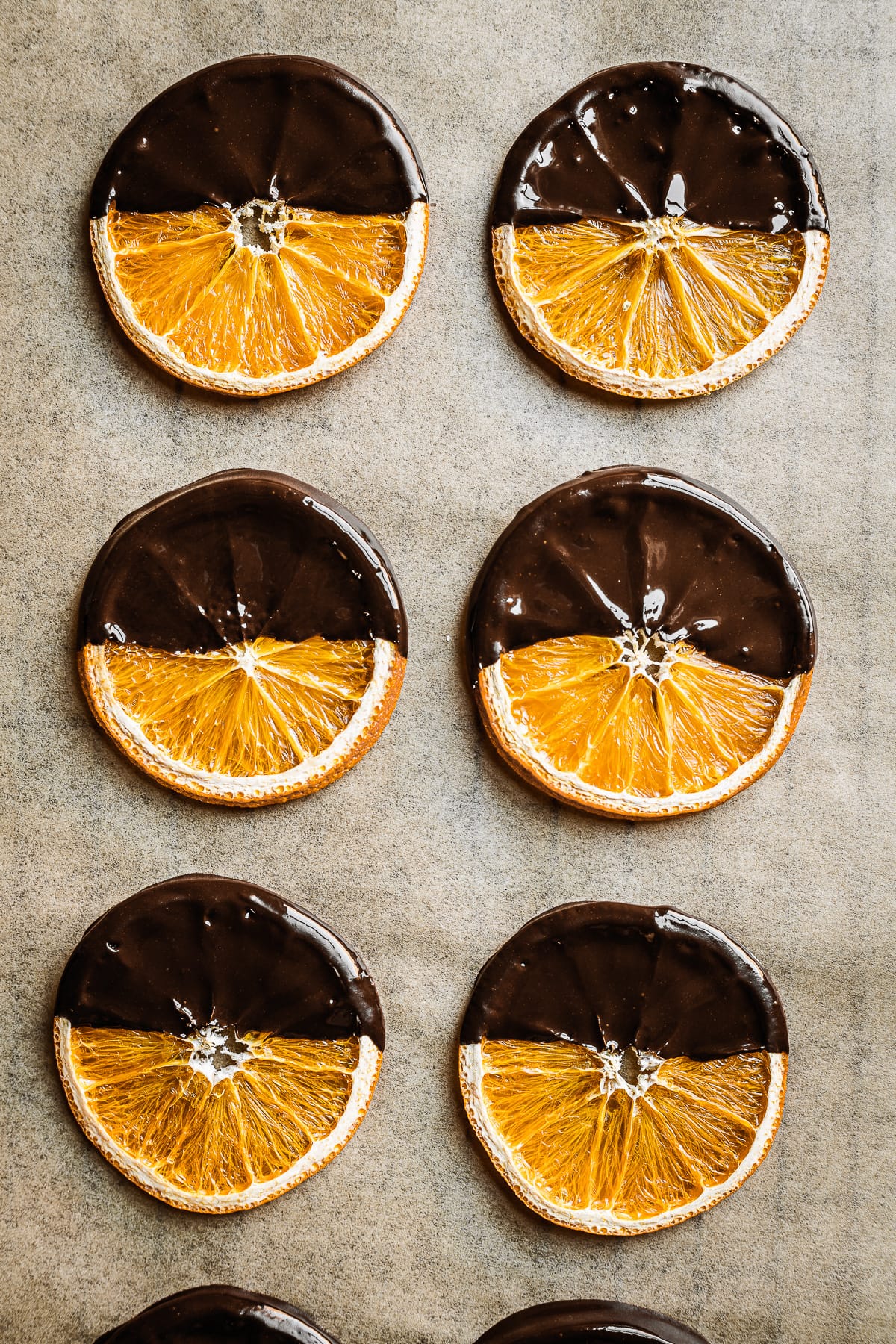 Dried orange slices dipped in dark chocolate on brown parchment paper.