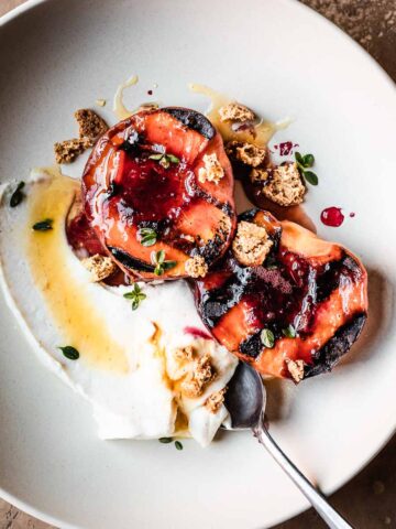 Grilled peaches with creamy cheese and honey in a low bowl with a spoon.