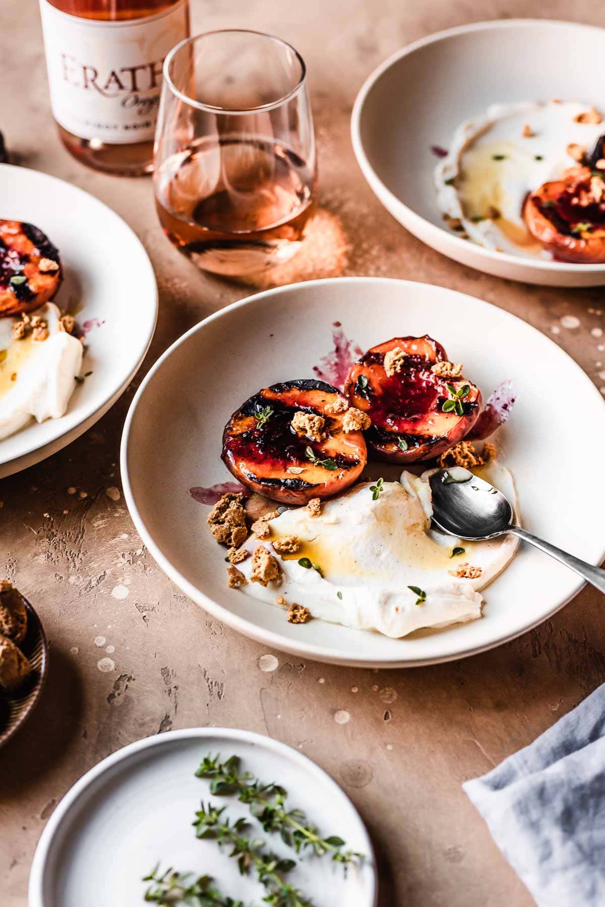 Bowls of grilled peaches with mascarpone cream and honey on a tan table with a glass of rose wine.