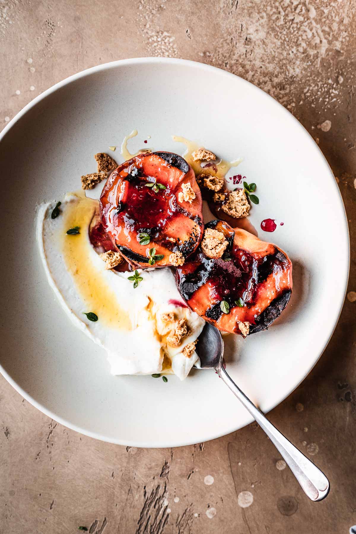 Grilled peaches with creamy cheese and honey in a low bowl with a spoon.