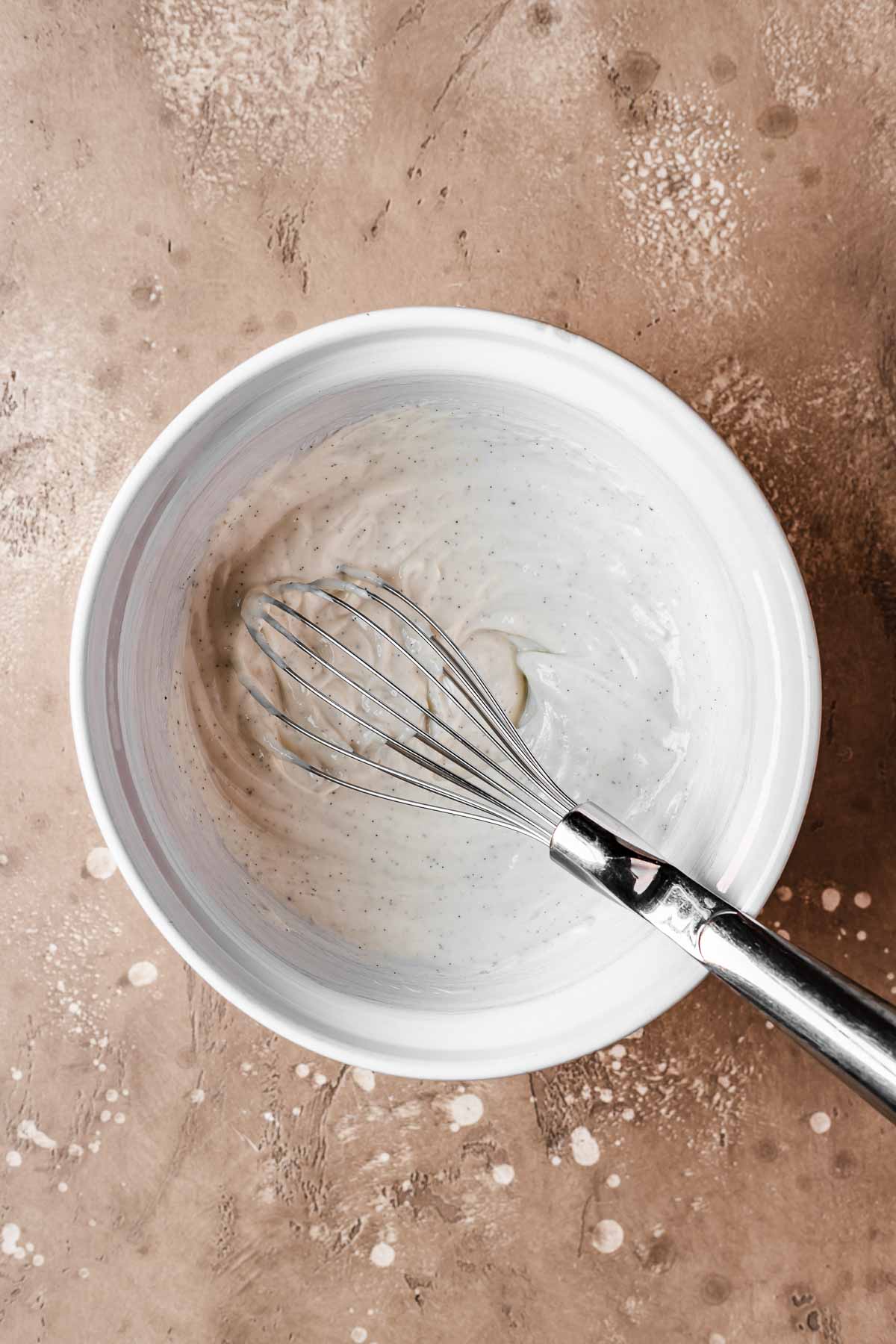 A bowl of greek yogurt and vanilla bean with a whisk resting inside.