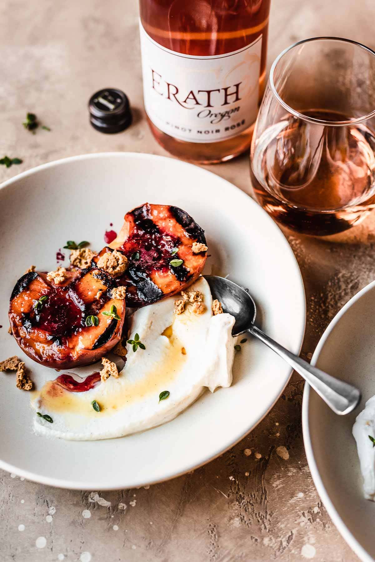 A bowl of grilled peaches with mascarpone cheese and honey with a glass of rose wine nearby.