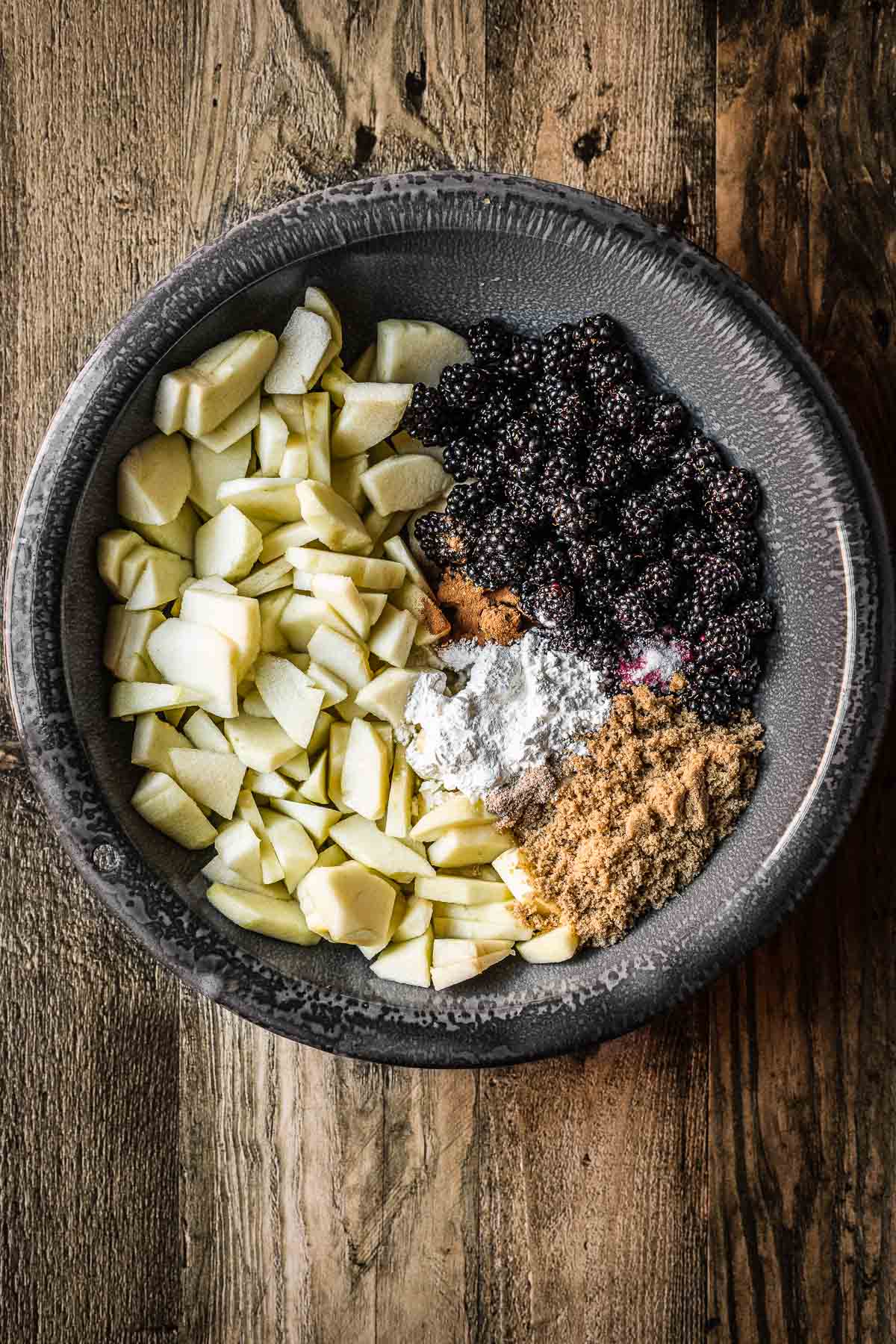 A rustic metal bowl of chopped apples, blackberries and other ingredients before mixing them together.