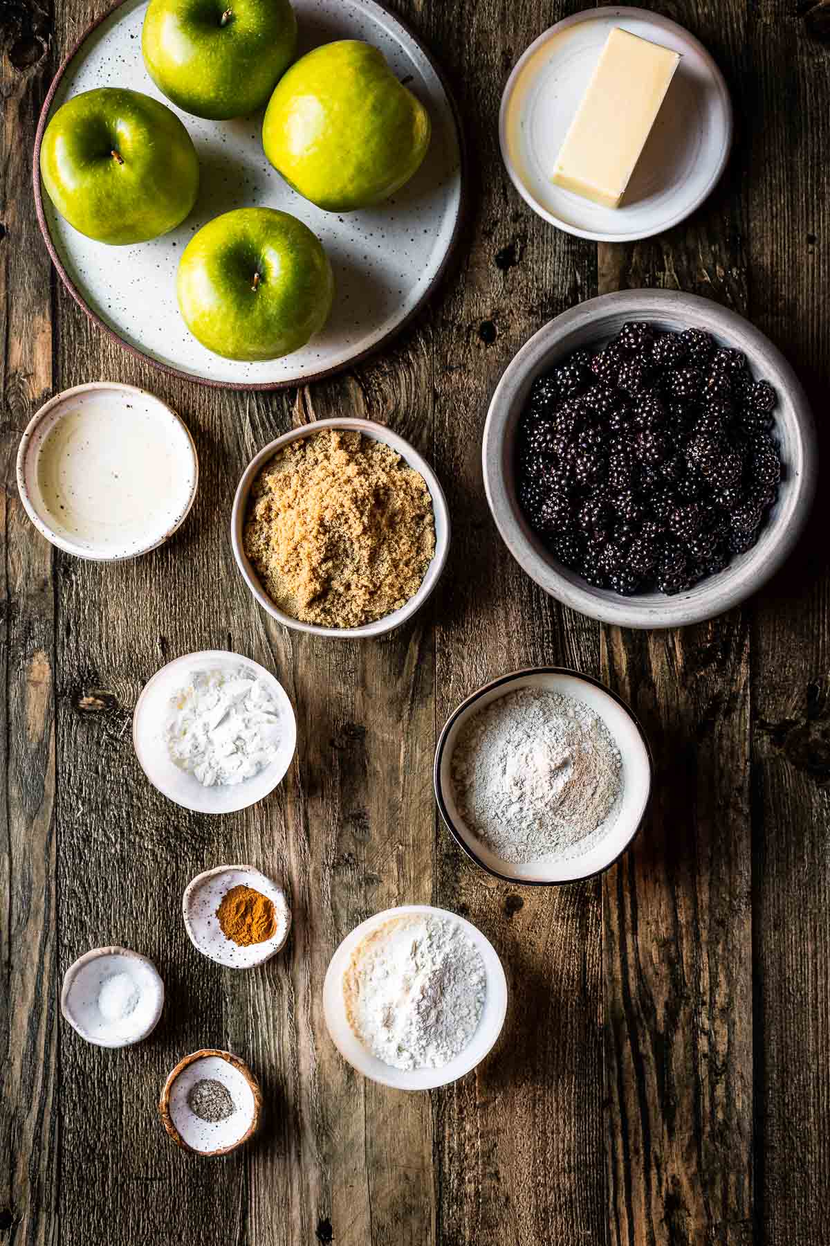 Ingredients for a berry apple crumble in bowls and plates on a rustic wooden tabletop.