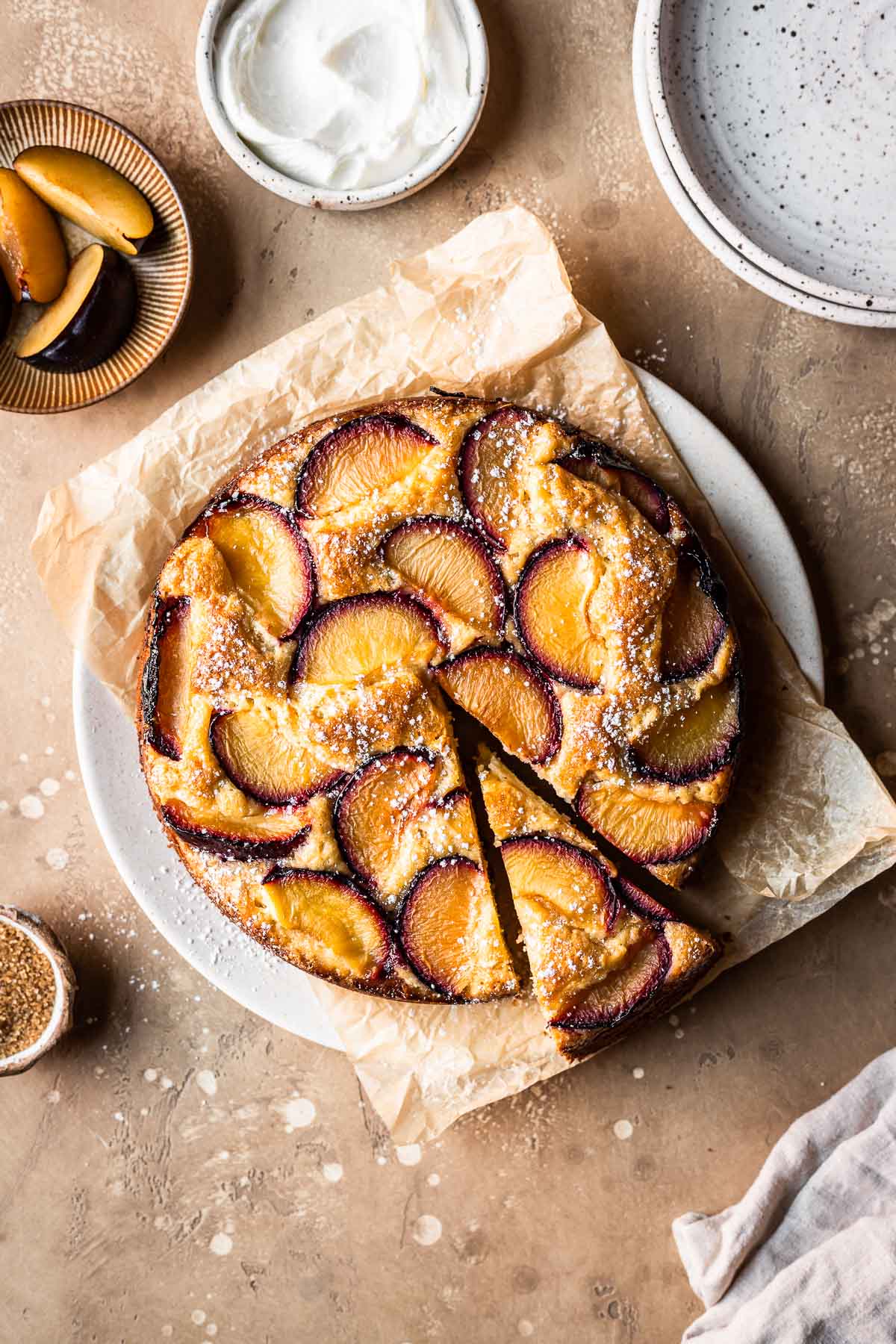 Baked plum cake on a parchment lined plate with a slice cut.