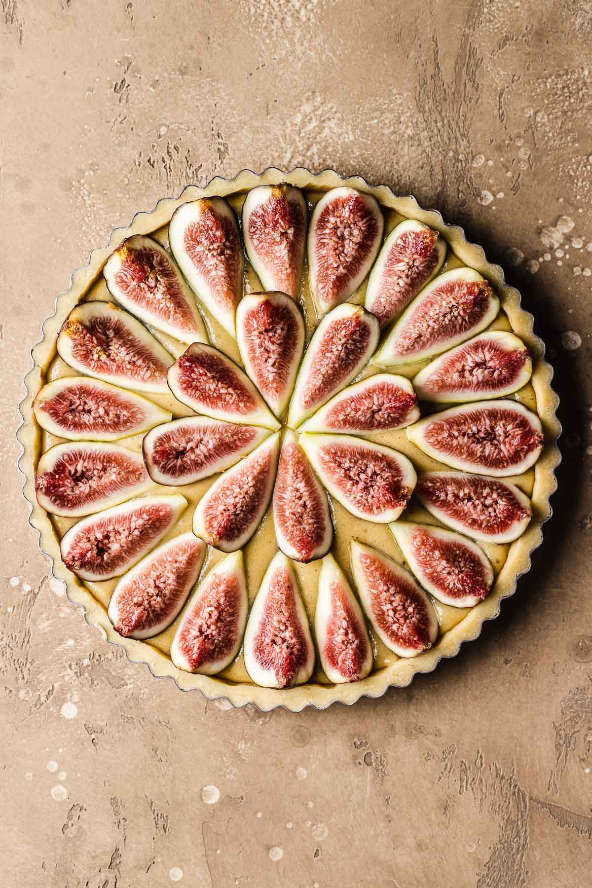 An unbaked French fig tart on a tan stone surface.