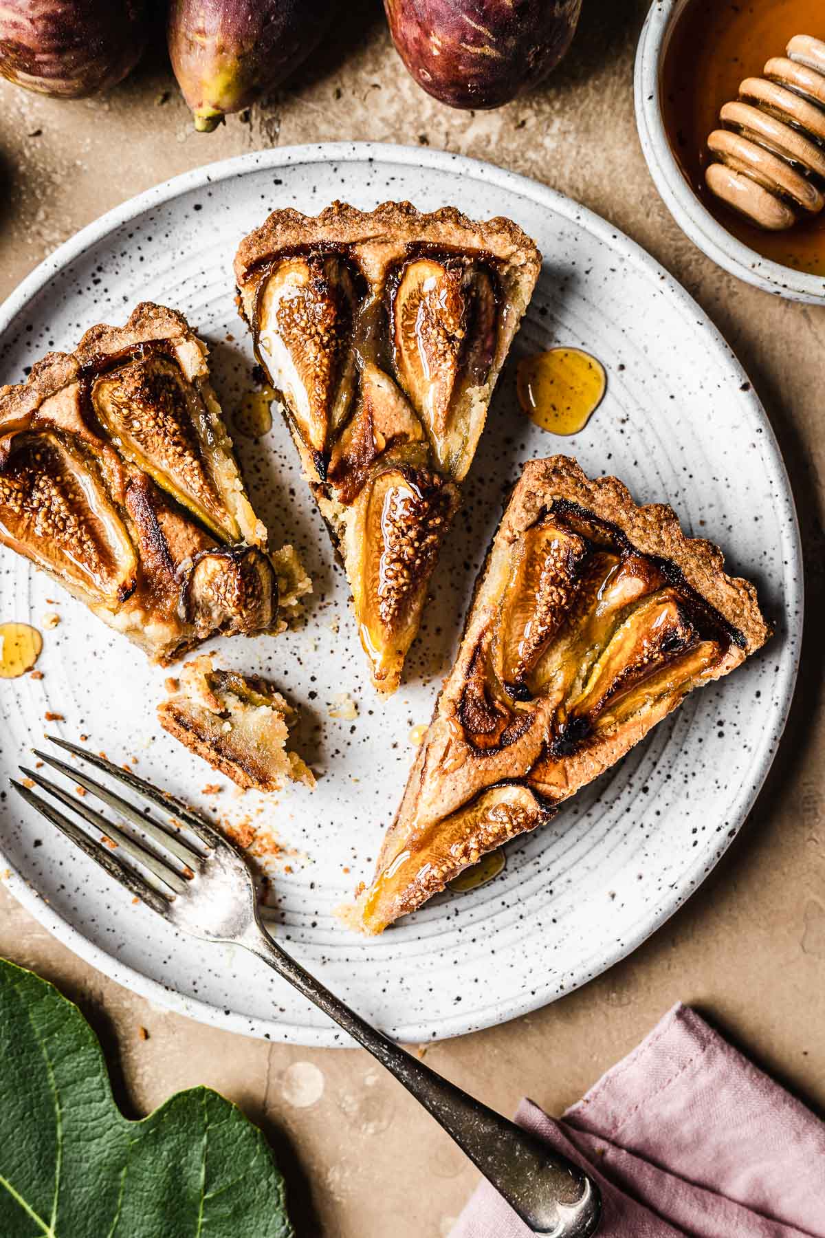 Three slices of tarte aux figues (fFrench fig tart) on a white speckled ceramic plate.