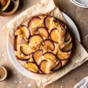 A baked plum yogurt cake on a parchment paper lined platter.