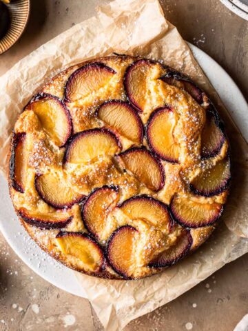 A baked plum yogurt cake on a parchment paper lined platter.